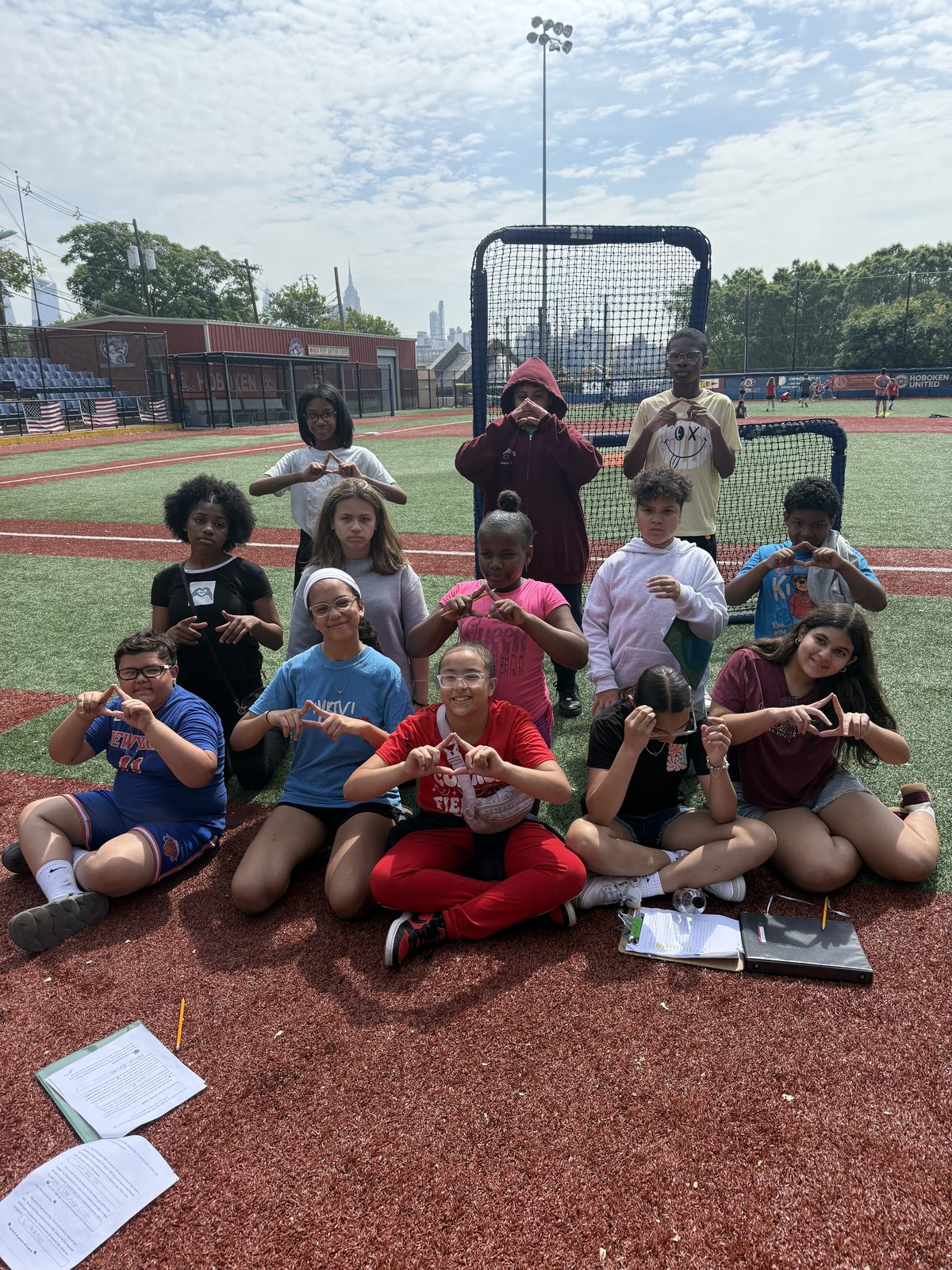 Fifth graders posing on a turf field with the NYC skyline behind them during the scavenger hunt